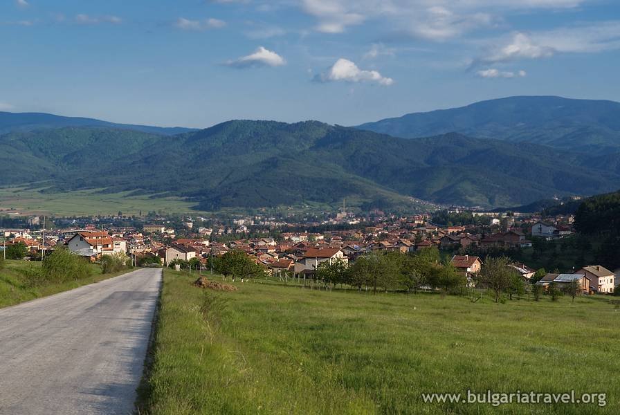 A winding road leading to a picturesque mountain village, surrounded by lush greenery and towering peaks.