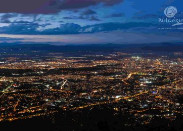 A breathtaking night view of the city, captured from a mountain peak. The city lights twinkle below, creating a mesmerizing sight.