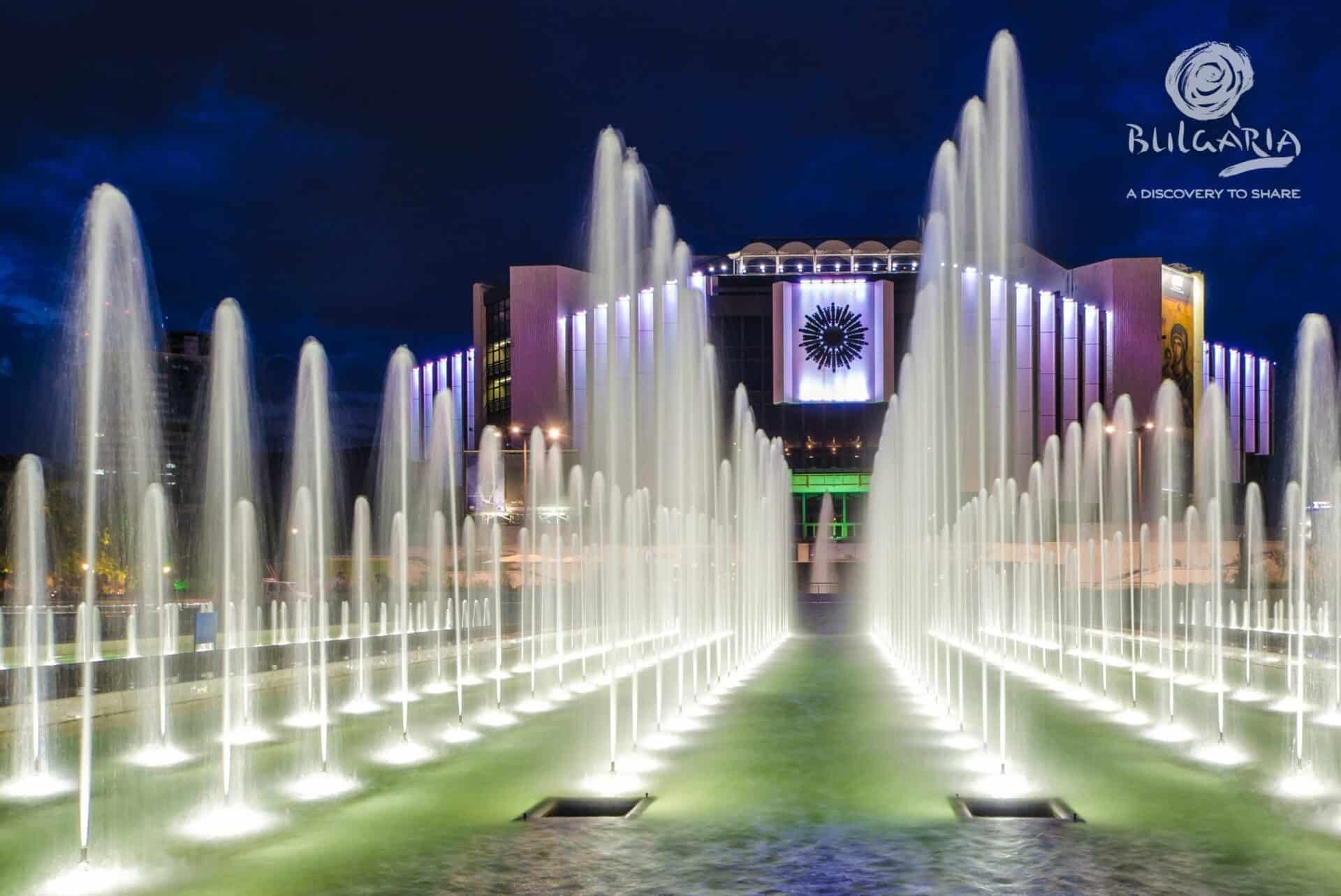 A grand fountain with water jets in front of a majestic building.