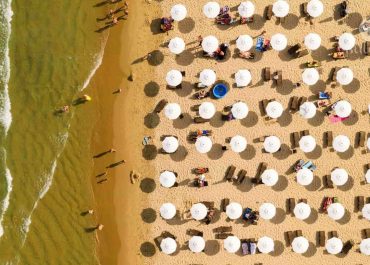 Aerial view of people enjoying a sunny day at the beach, with turquoise waters and golden sand.