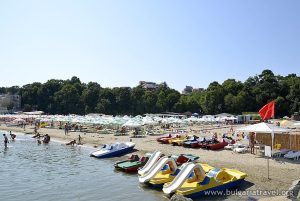 A crowded beach with numerous boats and people enjoying the sunny day by the sea.