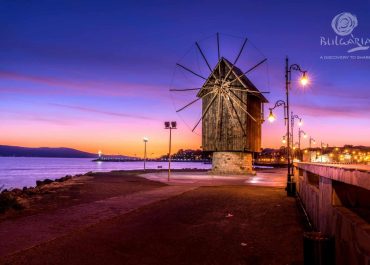Windmill on beach at sunset, purple sky.