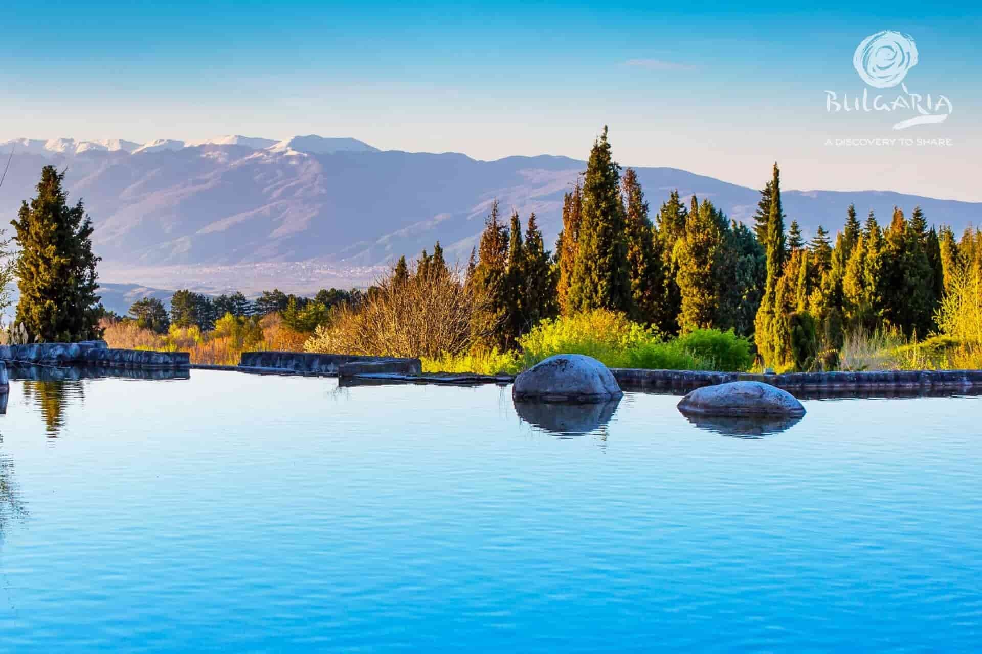 Scenic pool surrounded by rocks with majestic mountains in the background.