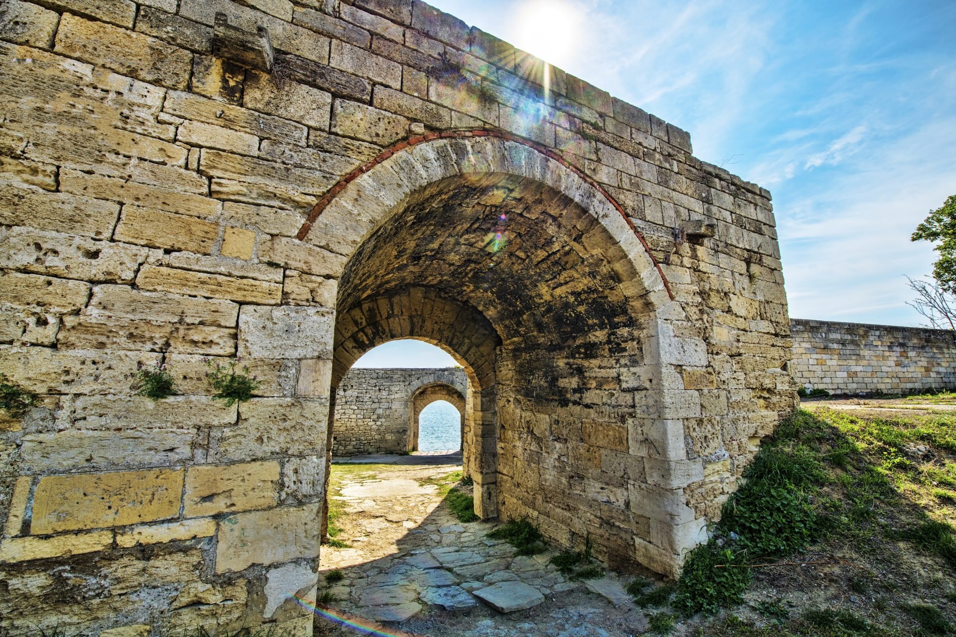 The sun illuminates an ancient stone wall through an archway, creating a beautiful and serene scene.