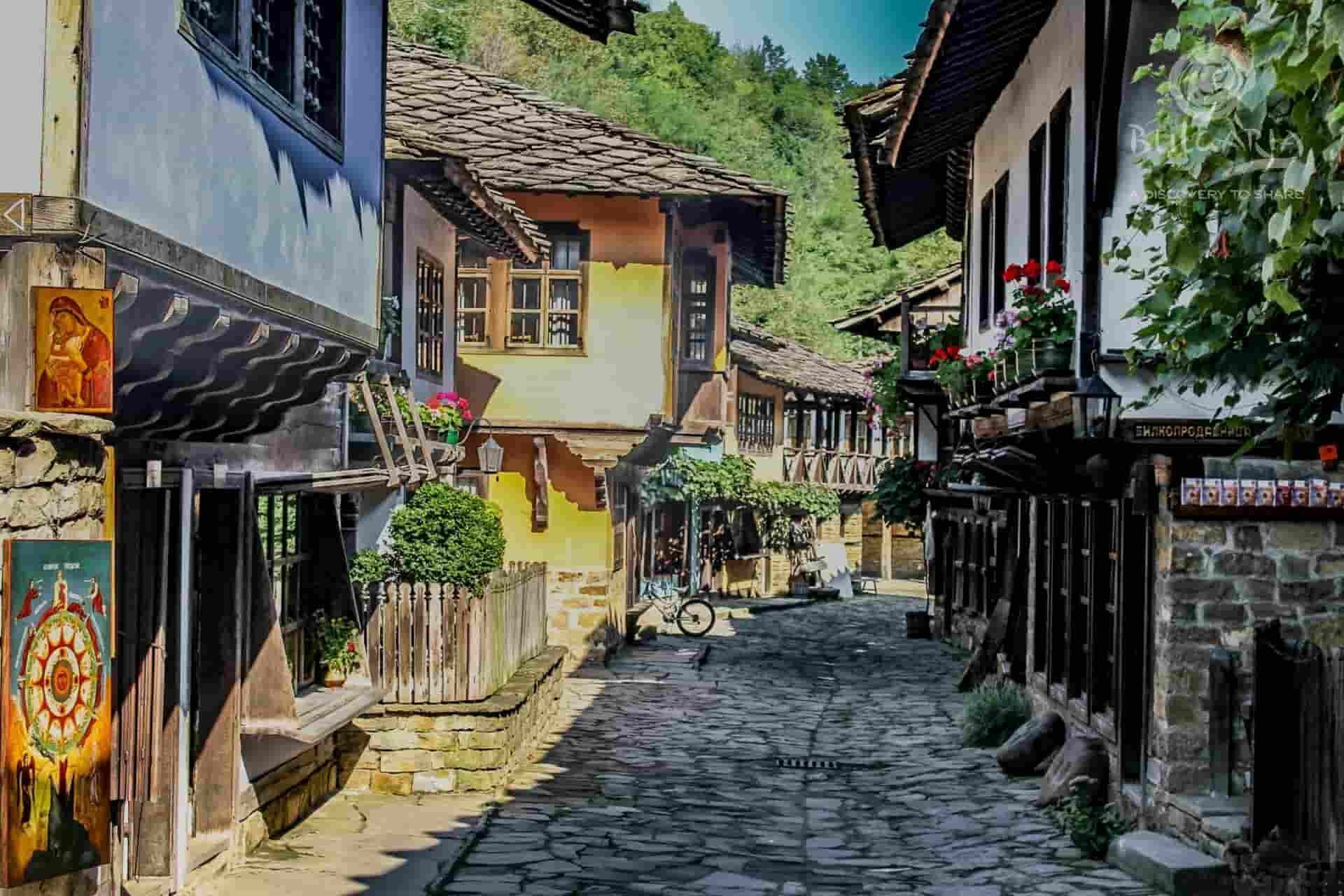 A quaint village street with cobblestones, surrounded by charming buildings and greenery